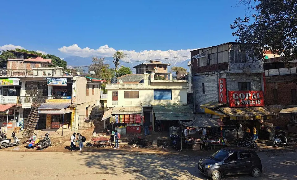 Shops along the main road at Rait, near Shahpur, with snow peaks beyond the roofs